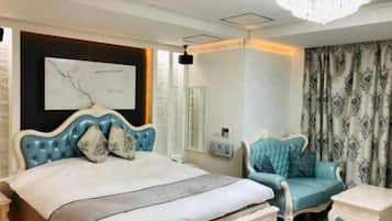 A bedroom with a large bed, a chair, a bedside table, a chandelier, and a wall-mounted artwork.