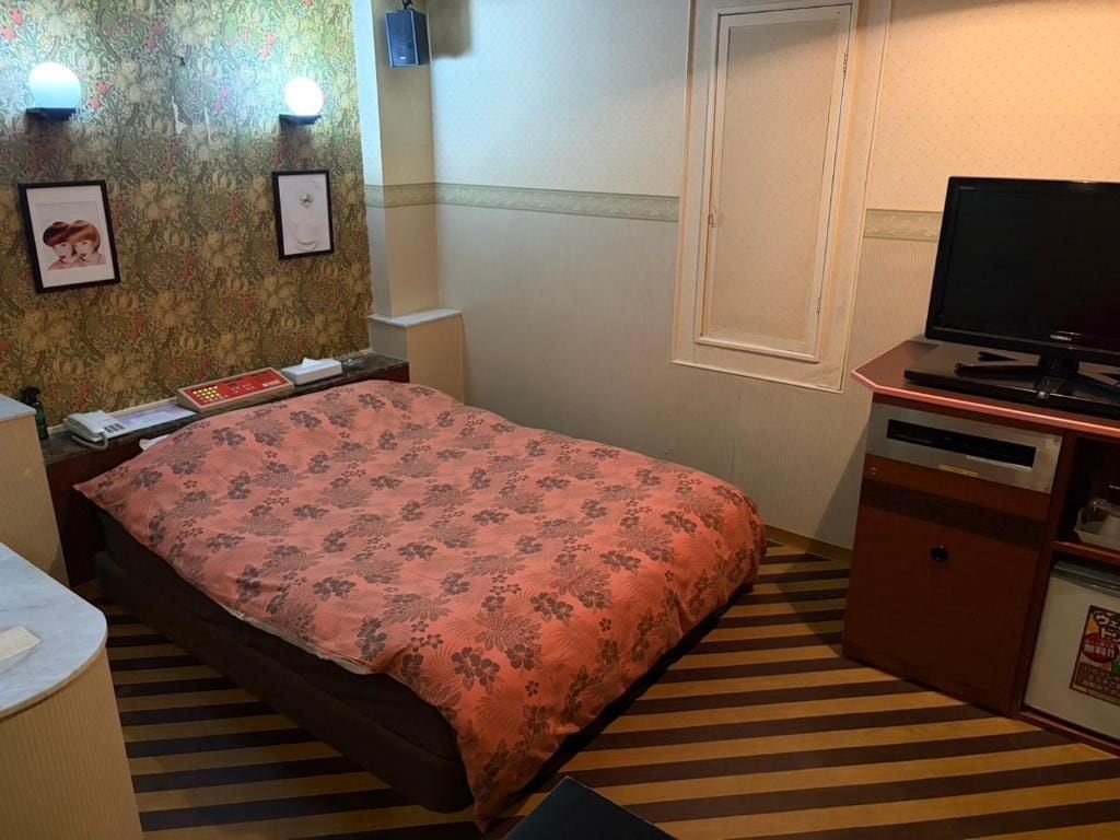 A hotel room with a bed, bedside table, lamp, television, and a small cabinet.