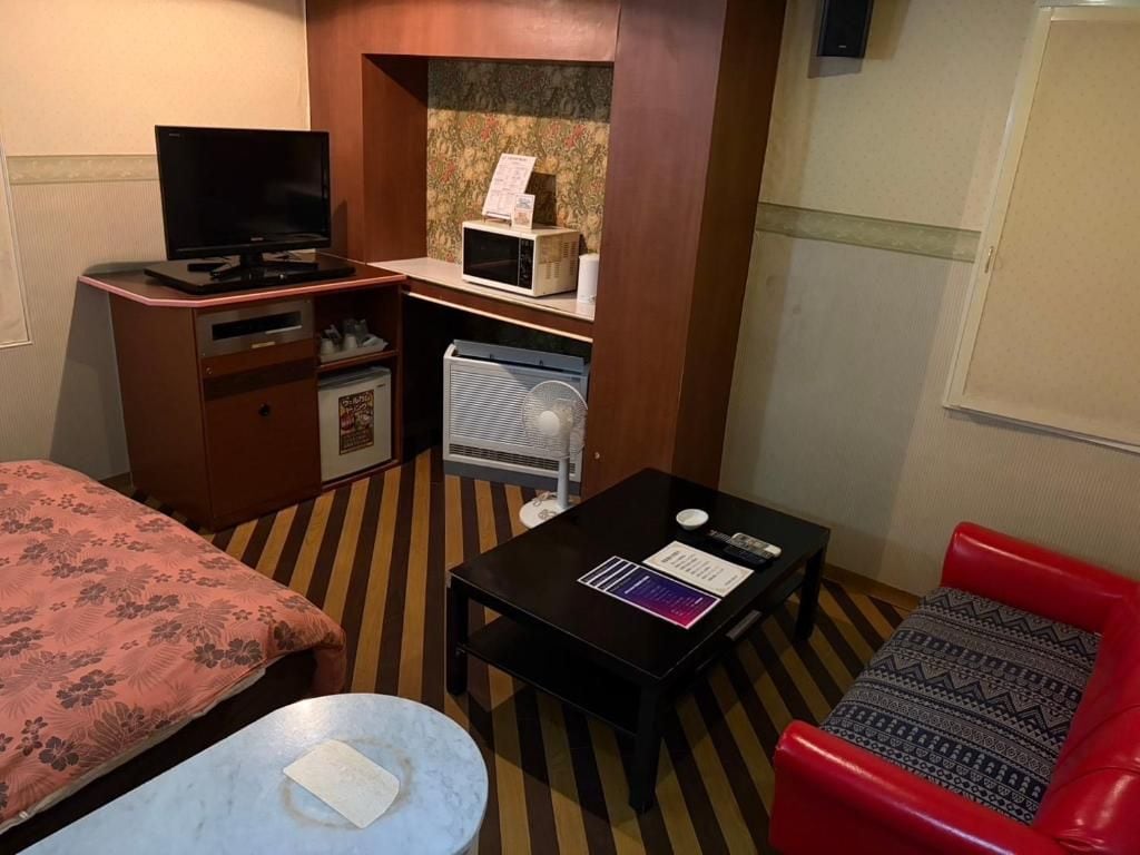Habitación de hotel con cama, escritorio con computadora, refrigerador pequeño, microondas y una silla roja.