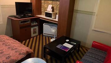 Habitación de hotel con cama, escritorio con computadora, refrigerador pequeño, microondas y una silla roja.