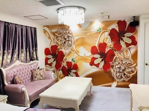 A room with a tufted sofa, a white coffee table, and a wall with floral artwork.