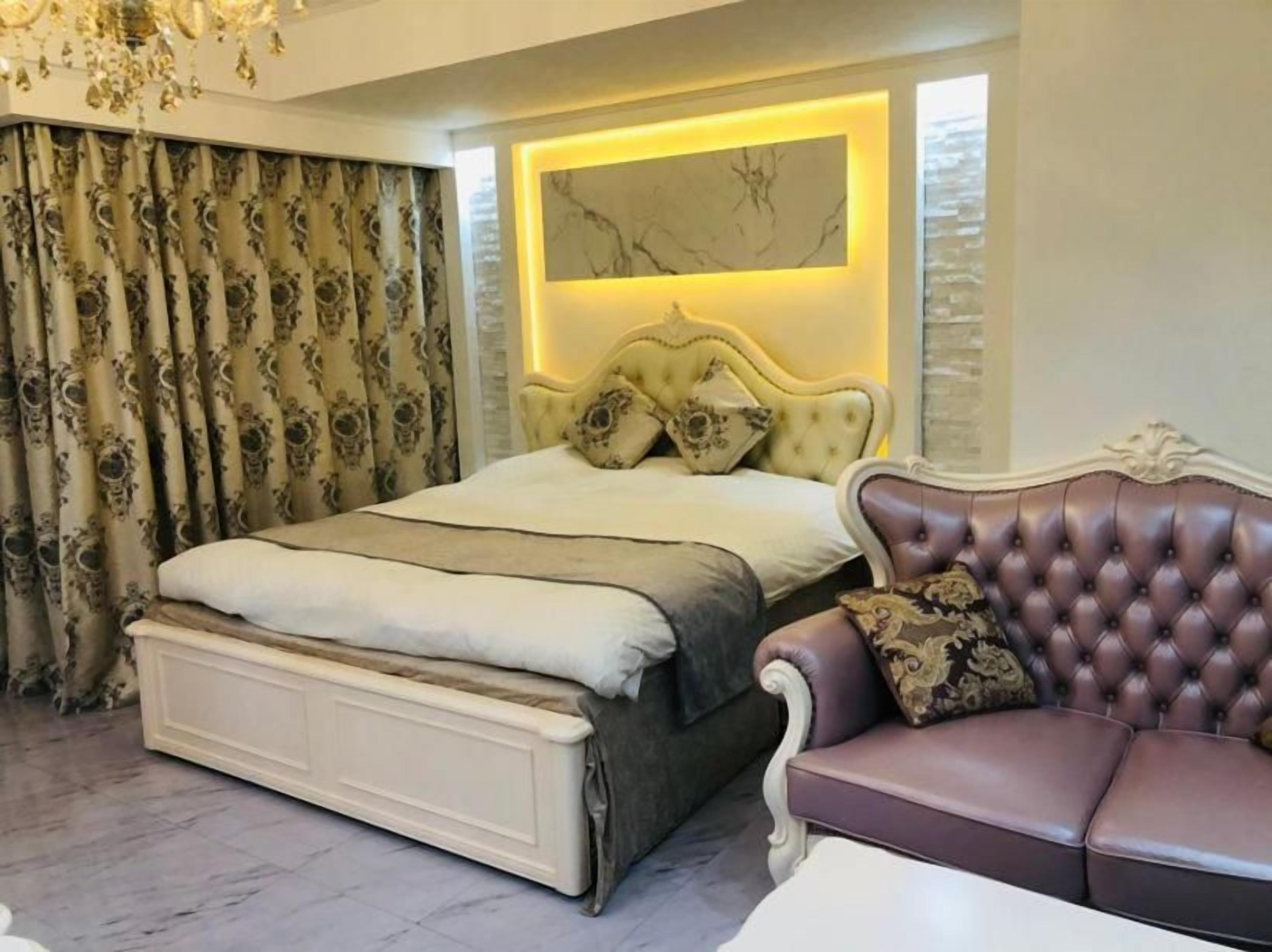 A bedroom with a large bed, a chaise lounge, and a decorative wall panel.