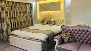 A bedroom with a large bed, a chaise lounge, and a decorative wall panel.