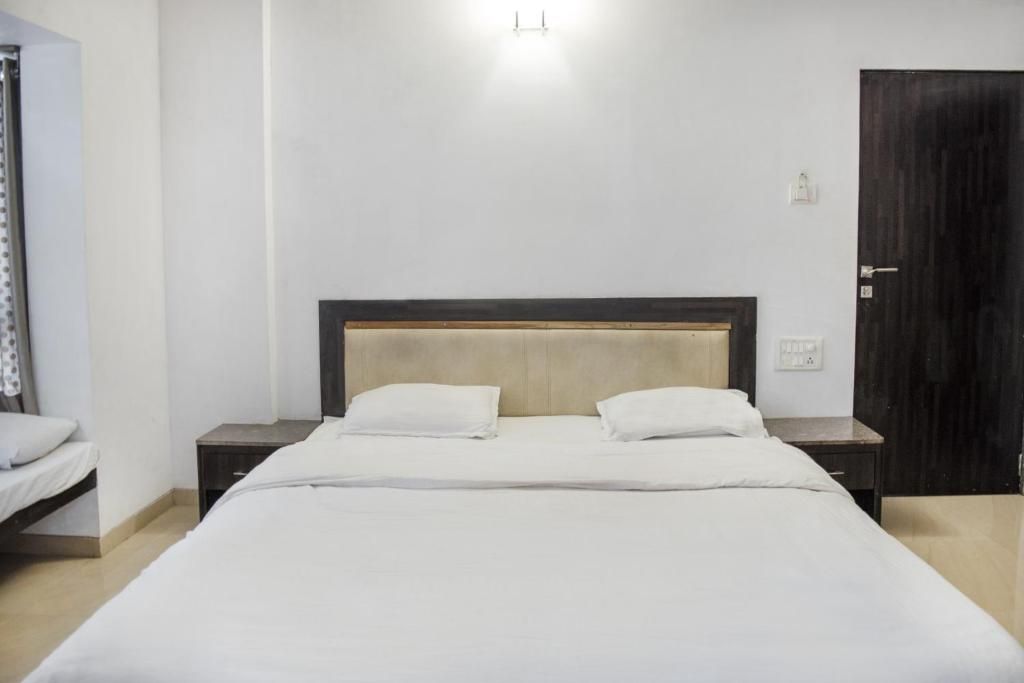A hotel room with a single bed, a nightstand, a wooden headboard, and a dark door.
