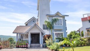 A two-story house with a prominent tower-like structure, a front porch, and a well-maintained garden. - Reveridge Skyinn 6BH Bungalow (Mahabaleshwar)
