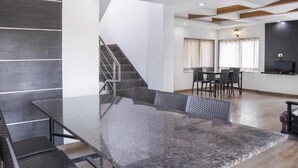 A modern interior with a dining area featuring a large table and chairs, a staircase, and a flat-screen TV mounted on the wall. - Reveridge Skyinn 6BH Bungalow (Mahabaleshwar)