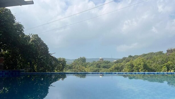 A clear swimming pool with a view of surrounding greenery and distant buildings. - Reveridge Skyinn 6BH Bungalow (Mahabaleshwar)