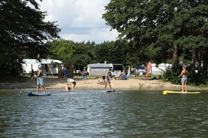 A lakeside scene with people paddleboarding, a sandy beach, and RVs parked nearby. - Trailer in Jabel with swimming pool (Jabel)