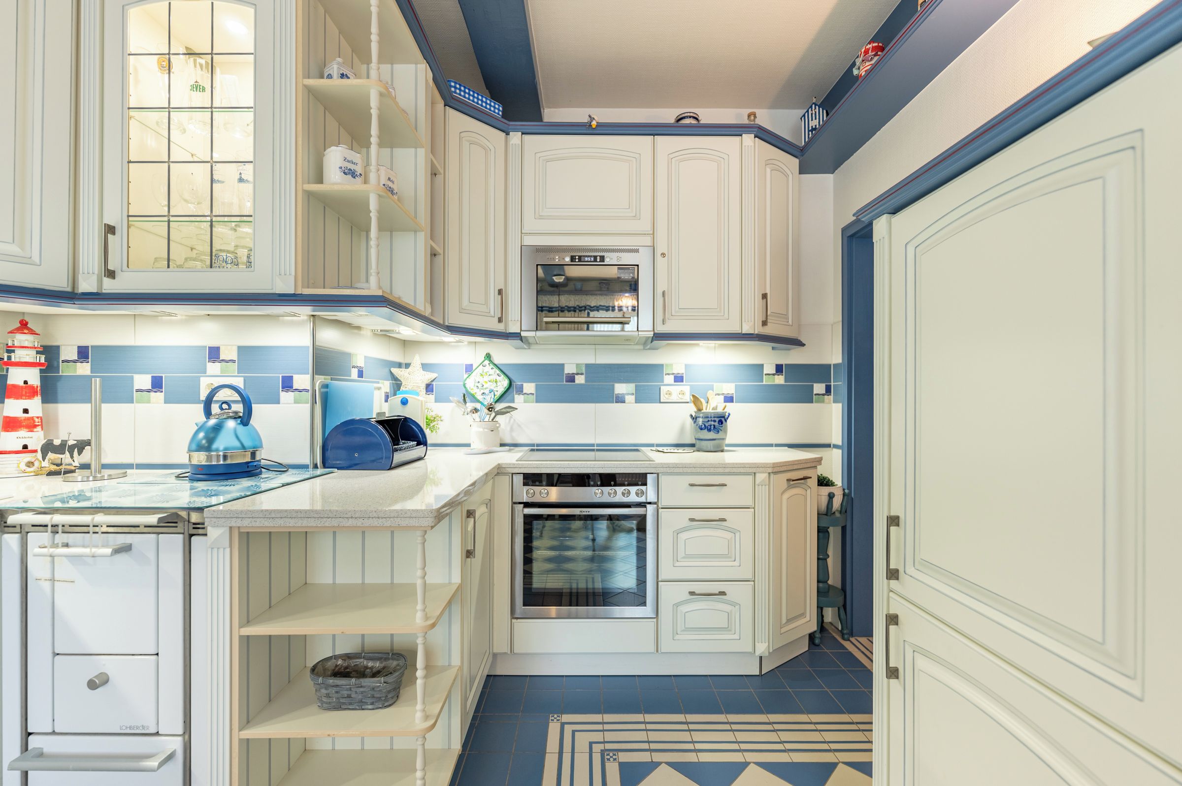 Une cuisine avec des meubles blancs, un dosseret carrelé aux motifs bleus et blancs, et une cuisinière.