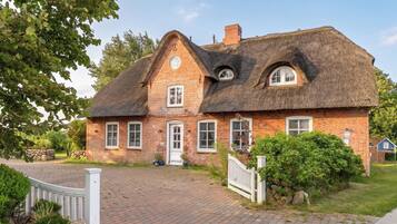Ein traditionelles Backsteinhaus mit Strohdach, einer Veranda und einem kleinen Garten.