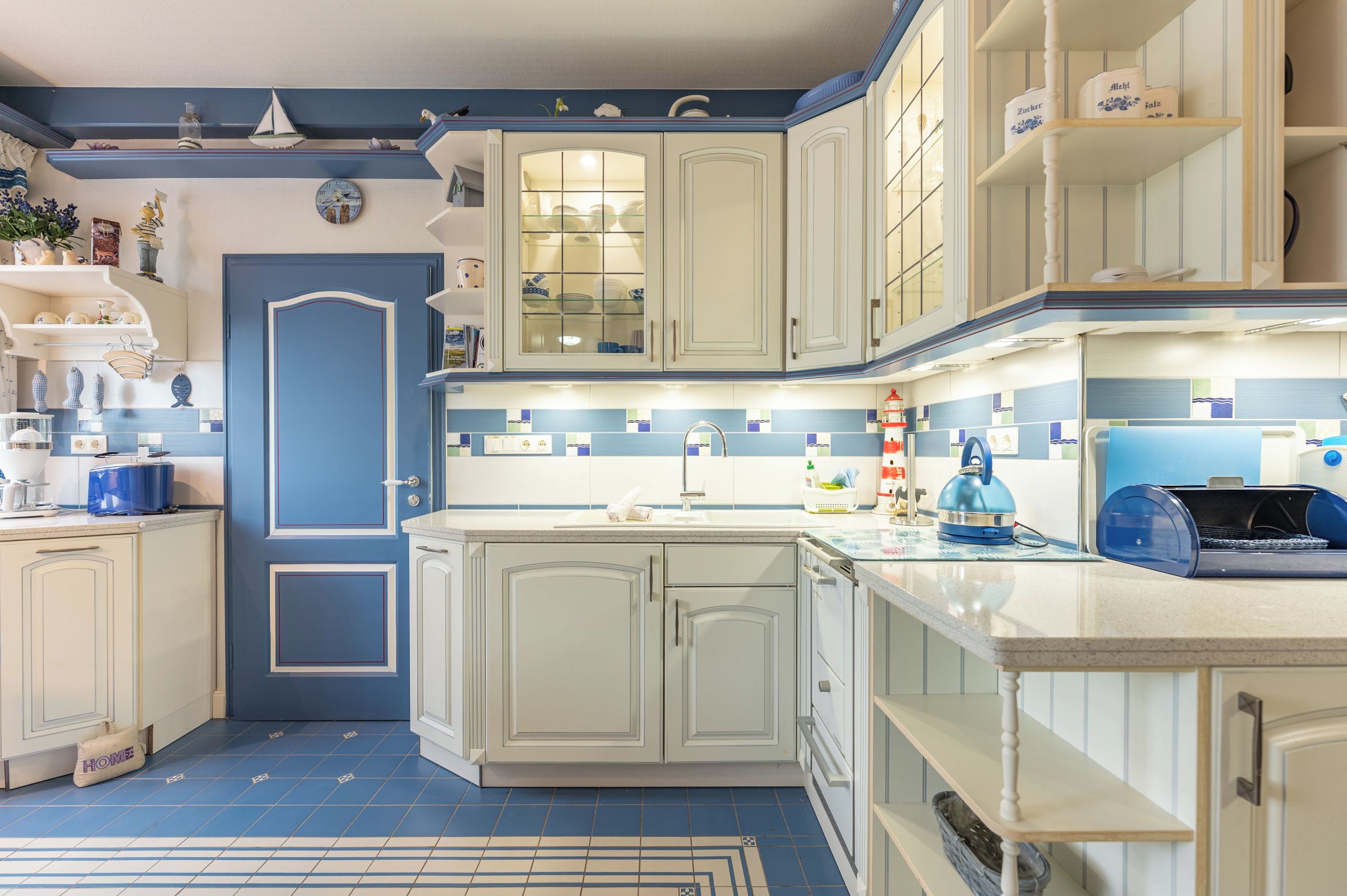 A kitchen with white cabinets, a blue door, and a tiled backsplash.