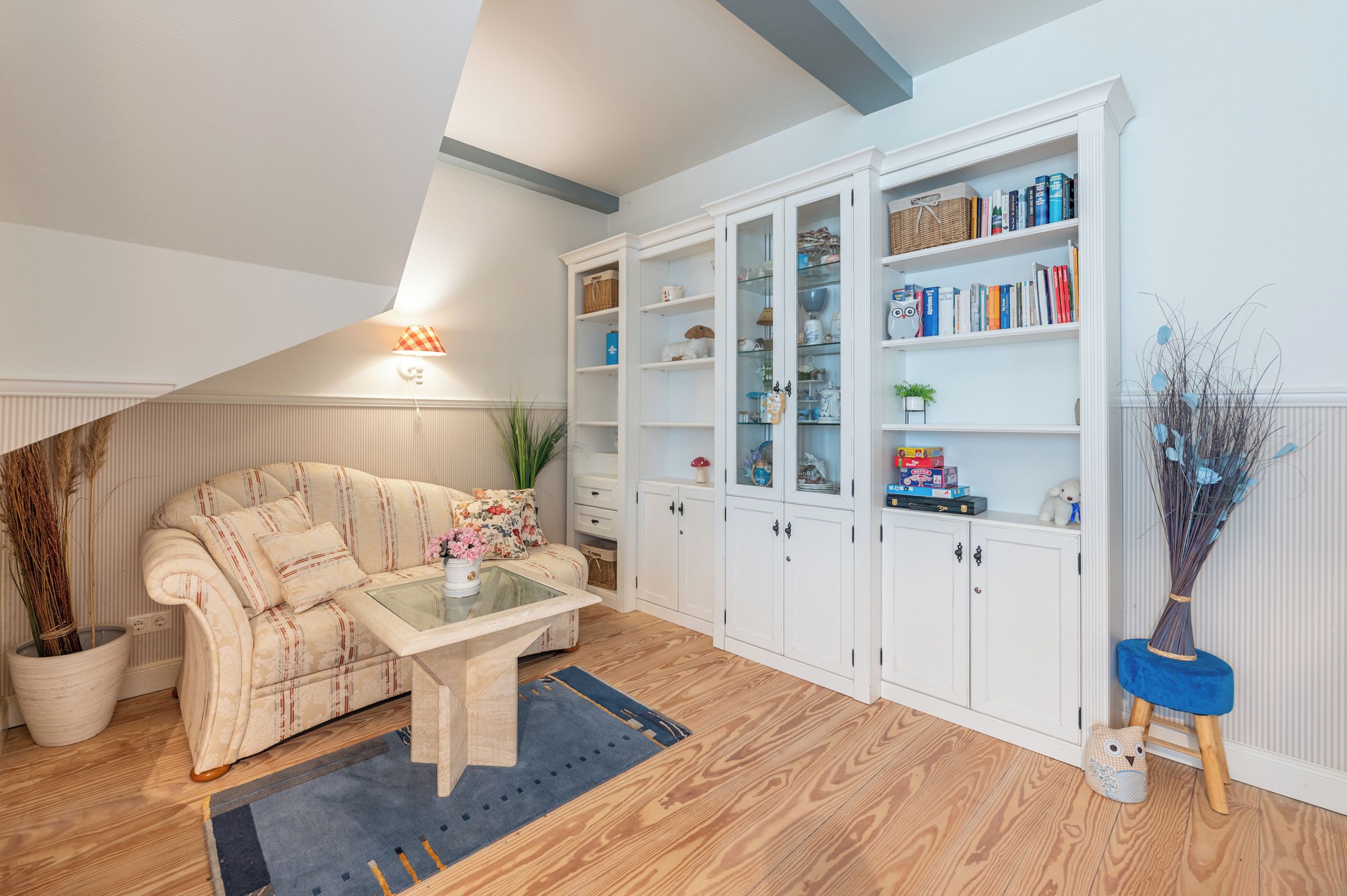 Ein gemütliches Wohnzimmer mit einer Couch, einem Couchtisch und einem Bücherregal, das mit Büchern und Dekoration gefüllt ist.