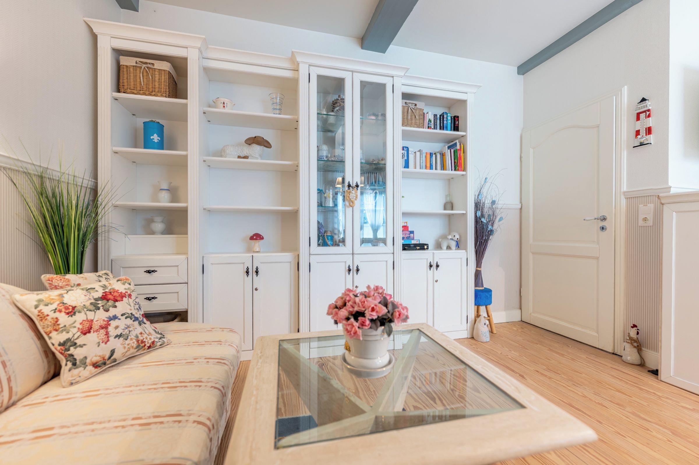 A living room with a sofa, a coffee table with a vase, and white shelving units with various items.