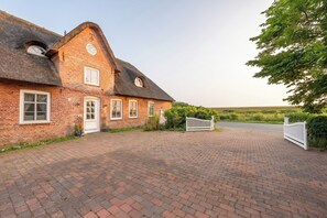 A brick house with a thatched roof, a white gate, and a paved driveway.