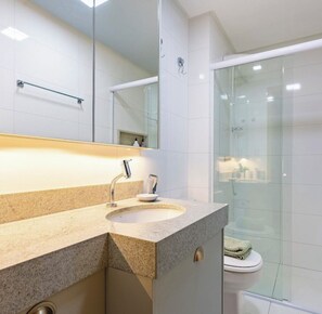 Une salle de bain moderne avec un comptoir en granit, un lavabo, un miroir et une cabine de douche en verre.