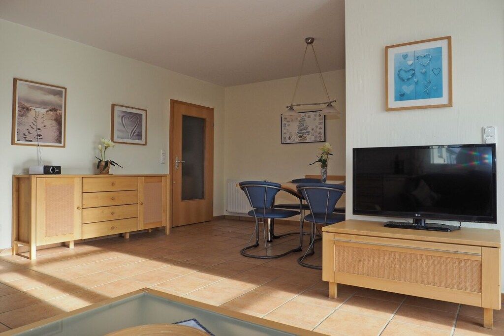 Un salon comprenant un téléviseur, un meuble en bois, une table à manger avec des chaises et des œuvres d’art accrochées aux murs.