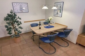 A dining area with a wooden table, four blue chairs, two pendant lights, a potted plant, and two framed pictures on the wall. - Dörmann "Haus Weser1" (Cuxhaven)