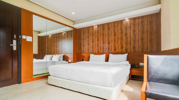 Une chambre d’hôtel moderne avec un grand lit, un mur revêtu de panneaux en bois, un miroir, une table de chevet et une chaise.
