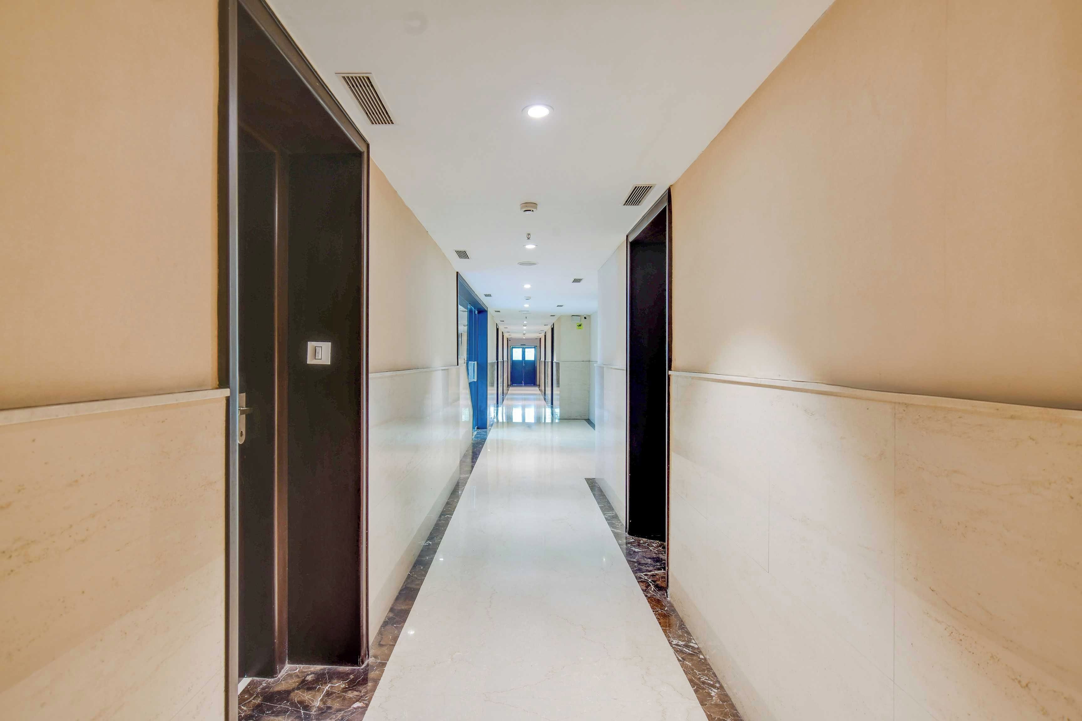 Un pasillo de hotel con piso de mármol, puertas a ambos lados y un largo camino hacia un extremo luminoso.