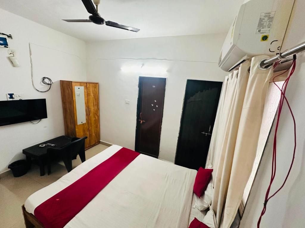 Una habitación de hotel con cama, escritorio, silla, televisor y ventilador de techo.