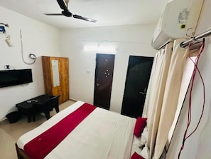A hotel room with a bed, a desk, a chair, a television, and a ceiling fan. - Hotel Deluxe (Hinjawadi)