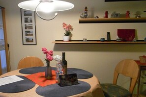 A dining area with a round table, placemats, a vase with flowers, a bottle, and a framed picture. - Holiday apartment with 1 bedroom (Werdum)