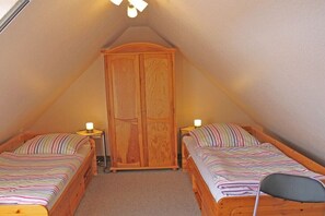 A small, cozy attic bedroom with two single beds, a wooden wardrobe, and a slanted ceiling. - Holiday apartment with 1 bedroom (Werdum)