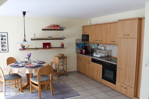 A compact kitchen with wooden cabinets, a microwave, and a dining area with a round table and chairs. - Holiday apartment with 1 bedroom (Werdum)