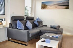 A modern living room with a grey sectional sofa, a coffee table, and a painting of a beach scene. - Sea lights Duhner Entrée 8 (Cuxhaven)