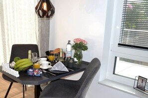 A breakfast setup with a table, chair, breakfast items, a vase with flowers, and a window with blinds. - Sea lights Duhner Entrée 8 (Cuxhaven)