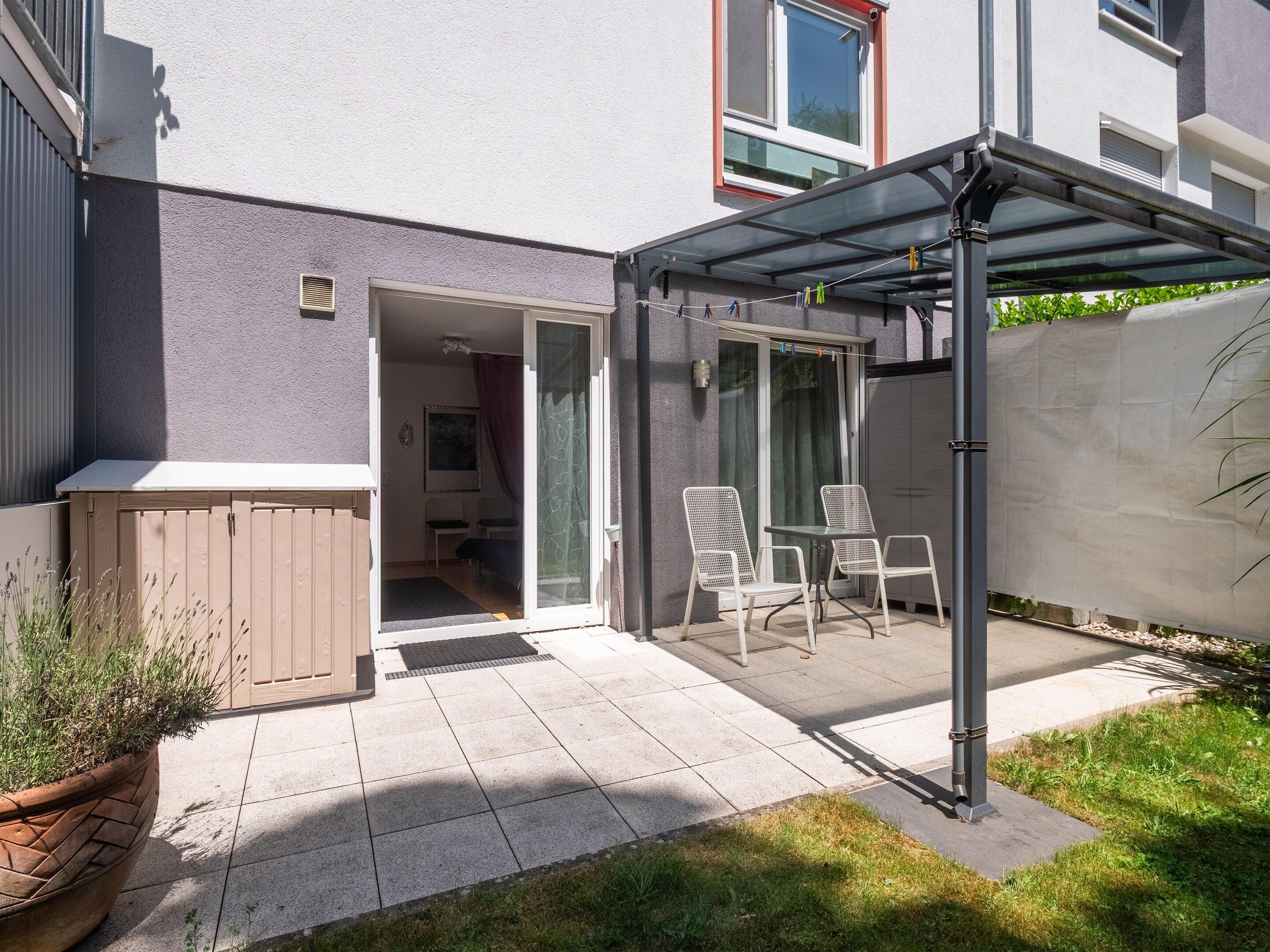 Eine Terrasse mit überdachter Sitzgruppe, einem Holzschrank und einem Blumentopf.