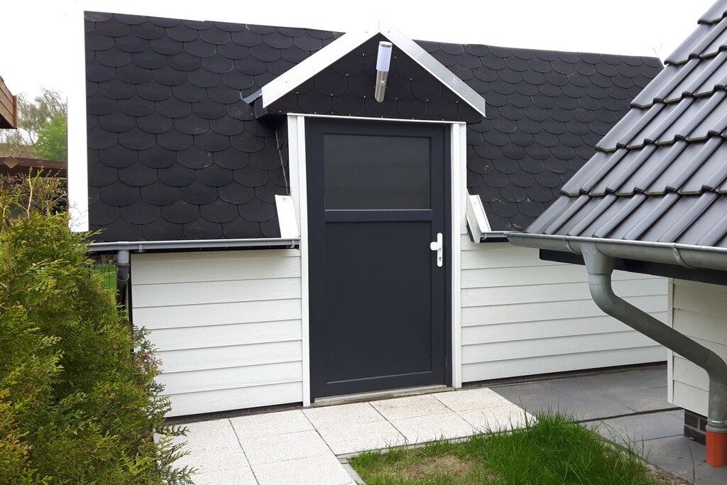 A residential building with a black door, white siding, and a dark roof.
