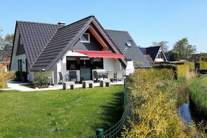 Ein Haus mit geneigtem Dach, einer roten Markise und einer kleinen Terrasse mit Gartenmöbeln.