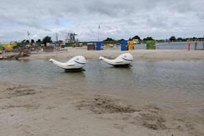 Ein Sandstrand mit zwei weißen, schwanenähnlichen Skulpturen im Wasser.
