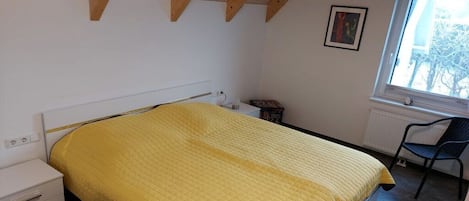 Ett sovrum med en säng, en stol, ett fönster och ett element.