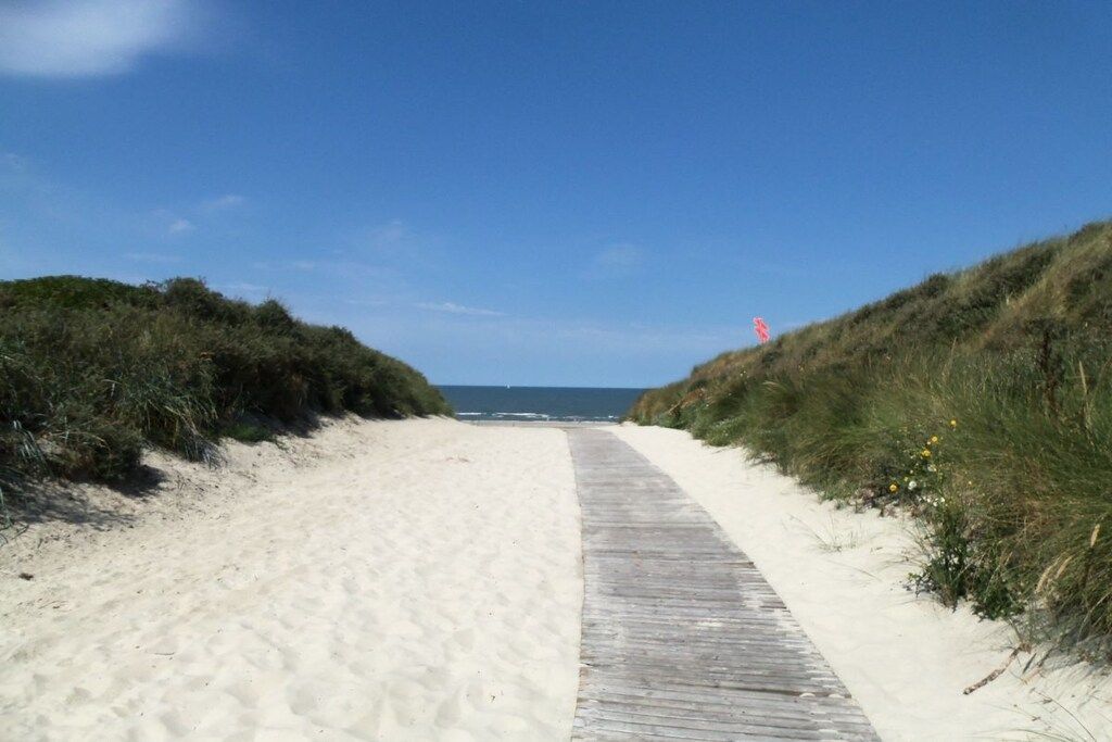 Ein Sandstrand mit einer hölzernen Promenade, die zum Meer führt.