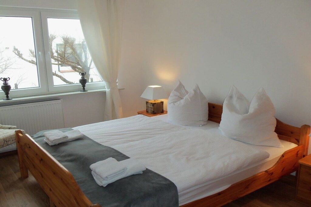 A neatly made bed with white linens, a bedside lamp, and a window with curtains.