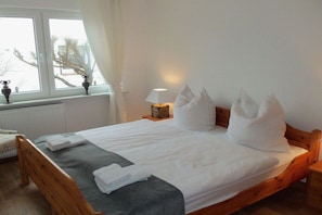 A neatly made bed with white linens, a bedside lamp, and a window with curtains. - Holiday home in Juist with swimming pool (Juist)