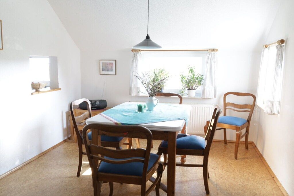 A dining area with a table, chairs, a hanging light fixture, a window with curtains, and a radiator.