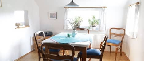 A dining area with a table, chairs, a hanging light fixture, a window with curtains, and a radiator.