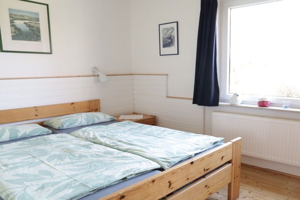 Ein Schlafzimmer mit einem hölzernen Bett, einem Nachttisch, einem Fenster mit Aussicht und zwei gerahmten Bildern an der Wand.