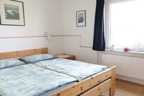 A bedroom with a wooden bed, a nightstand, a window with a view, and two framed pictures on the wall. - in the holiday home Deichblick (Norden)