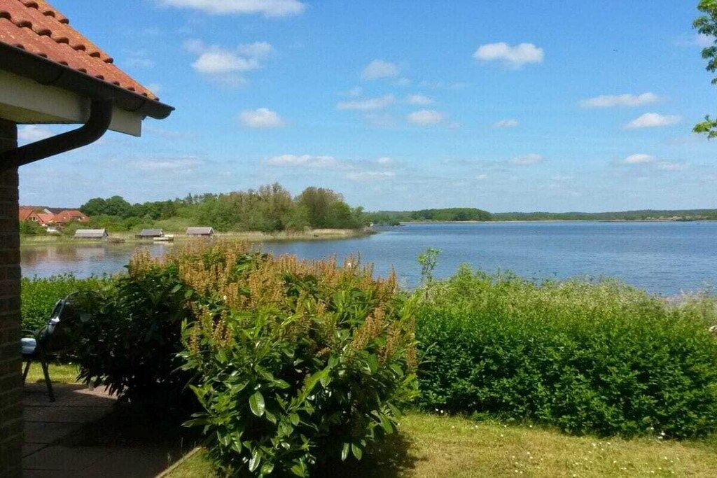 Uitzicht op een meer met een gebouw, een stoel en weelderige begroeiing.