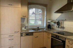Eine Küche mit eingebautem Geschirrspüler, Herd und einem Fenster mit Jalousien.