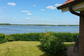 Blick auf einen See mit einer Wiese und einem Ziegelgebäude mit rotem Dach.