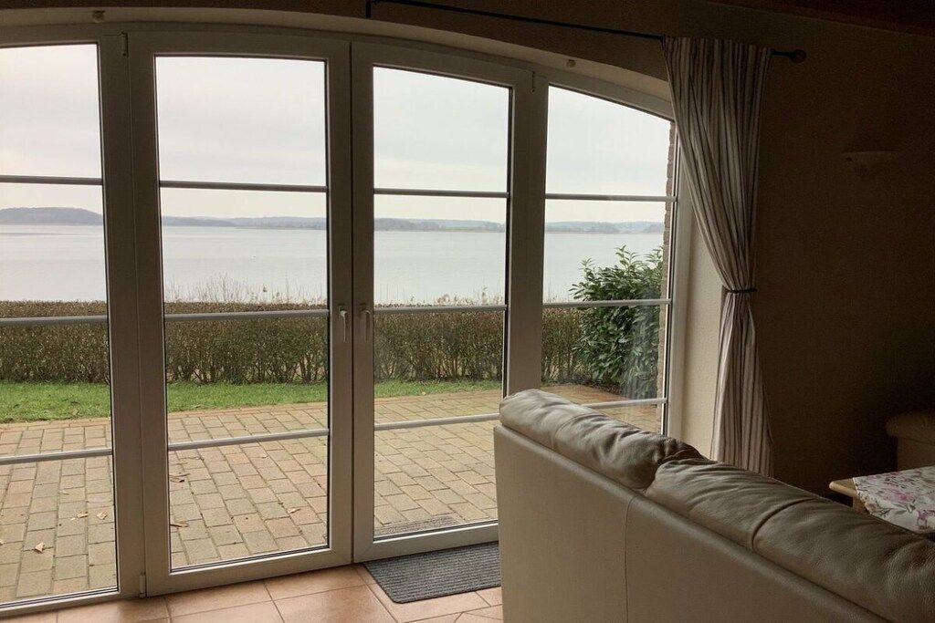 Een kamer met een schuifglazen deur die uitkomt op een terras met uitzicht op een waterpartij en het landschap in de verte.