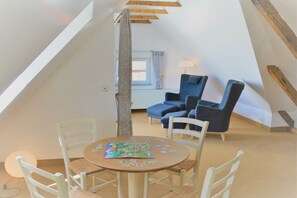 A cozy room with a sloped ceiling, a round table with chairs, and two blue armchairs. - with loggia in Haus Wittdün (Juist)