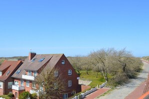 A residential building with a sloped roof, multiple windows, and a pathway leading to a grassy area. - with loggia in Haus Wittdün (Juist)