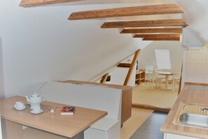 A compact kitchen with wooden beams, a dining area with a table and chairs, and a small kitchenette. - with loggia in Haus Wittdün (Juist)