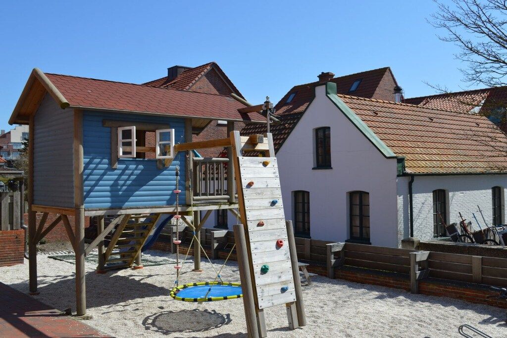 A playground with a climbing wall and a slide, surrounded by buildings with pitched roofs.